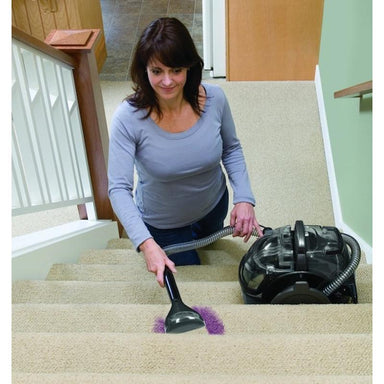 Woman cleaning stairs with Bissell BGU1451T bagged upright vacuum.